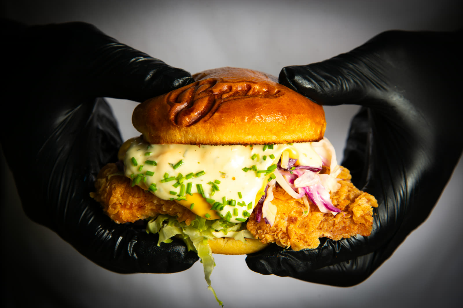 Burger de poulet frit tenu à deux mains gantées de noir